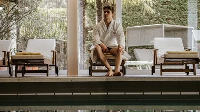 Man in bathrobe sitting on lounge chair next to indoor pool