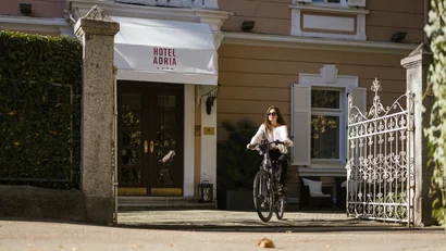 Woman riding a bicycle in front of Hotel Adria entrance on a sunny day