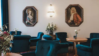 Elegant room with blue velvet chairs, wooden tables, and historical portrait paintings