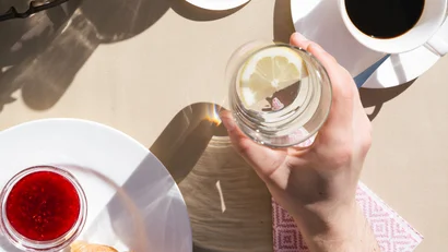 Breakfast table with croissant, coffee, water, and flowers in sunlight