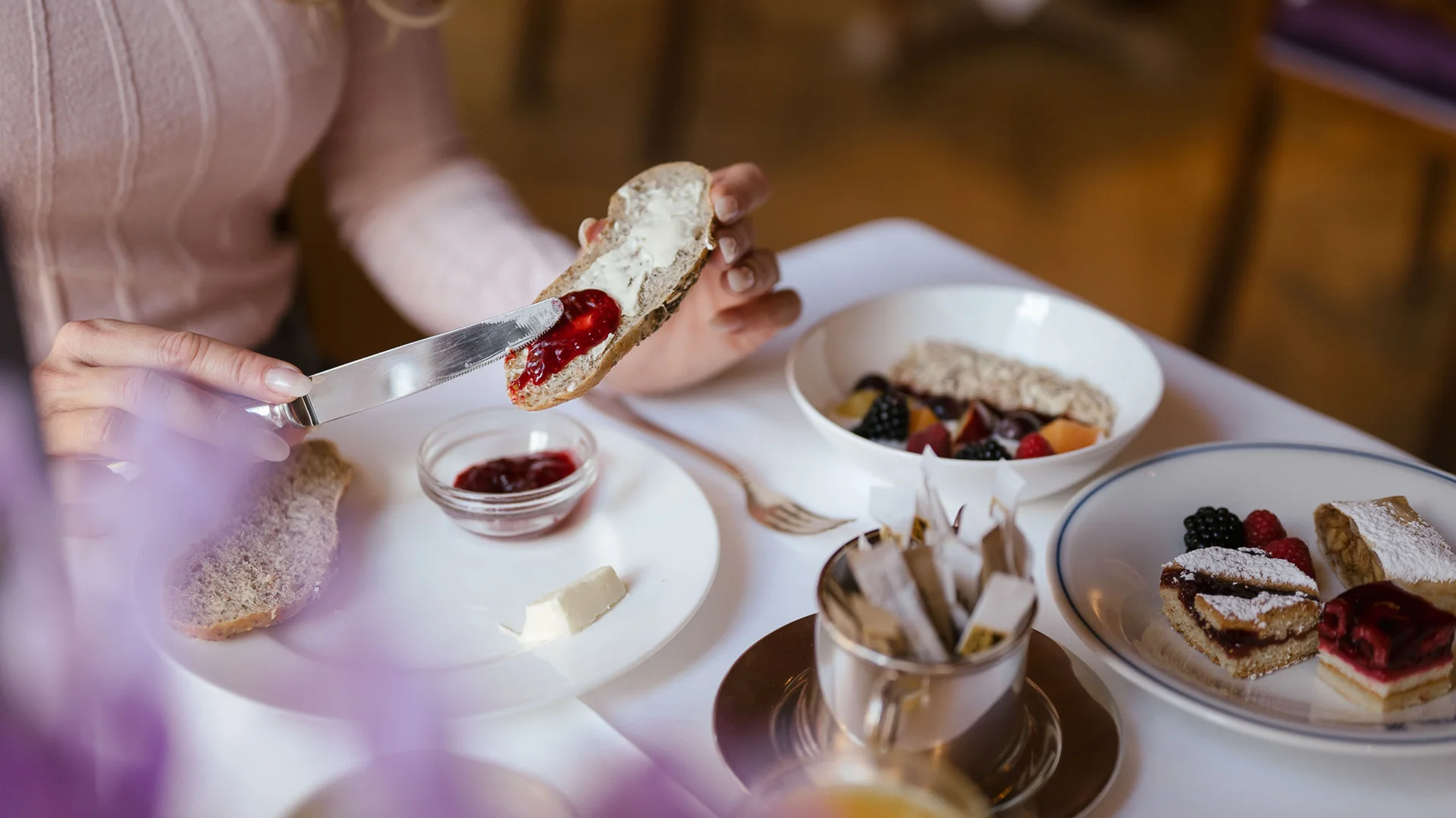 Person spreading jam on bread at a set breakfast table