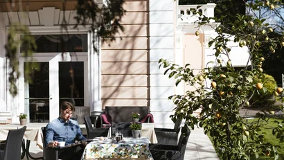 Man sitting outside on terrace in front of house with book and coffee