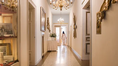 Woman in white dress walking down an elegant hallway with chandeliers