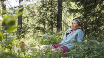 Woman relaxing barefoot sitting on grass in summer forest
