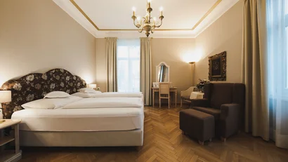 Elegant hotel room with two beds, armchairs, and chandelier