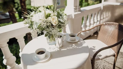Bouquet of flowers and two coffee cups on table on sunny balcony
