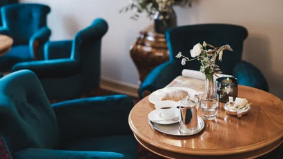 Cozy table with coffee, pastry, and vase in a room with blue armchairs