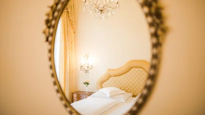 Reflection in mirror of elegant bright hotel room with white bed and chandelier