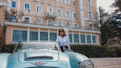 Woman beside a blue Austin Healey convertible in front of Hotel Adria