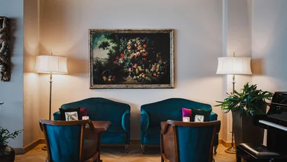 Cozy seating area with blue armchairs, floor lamps, and floral painting on wall