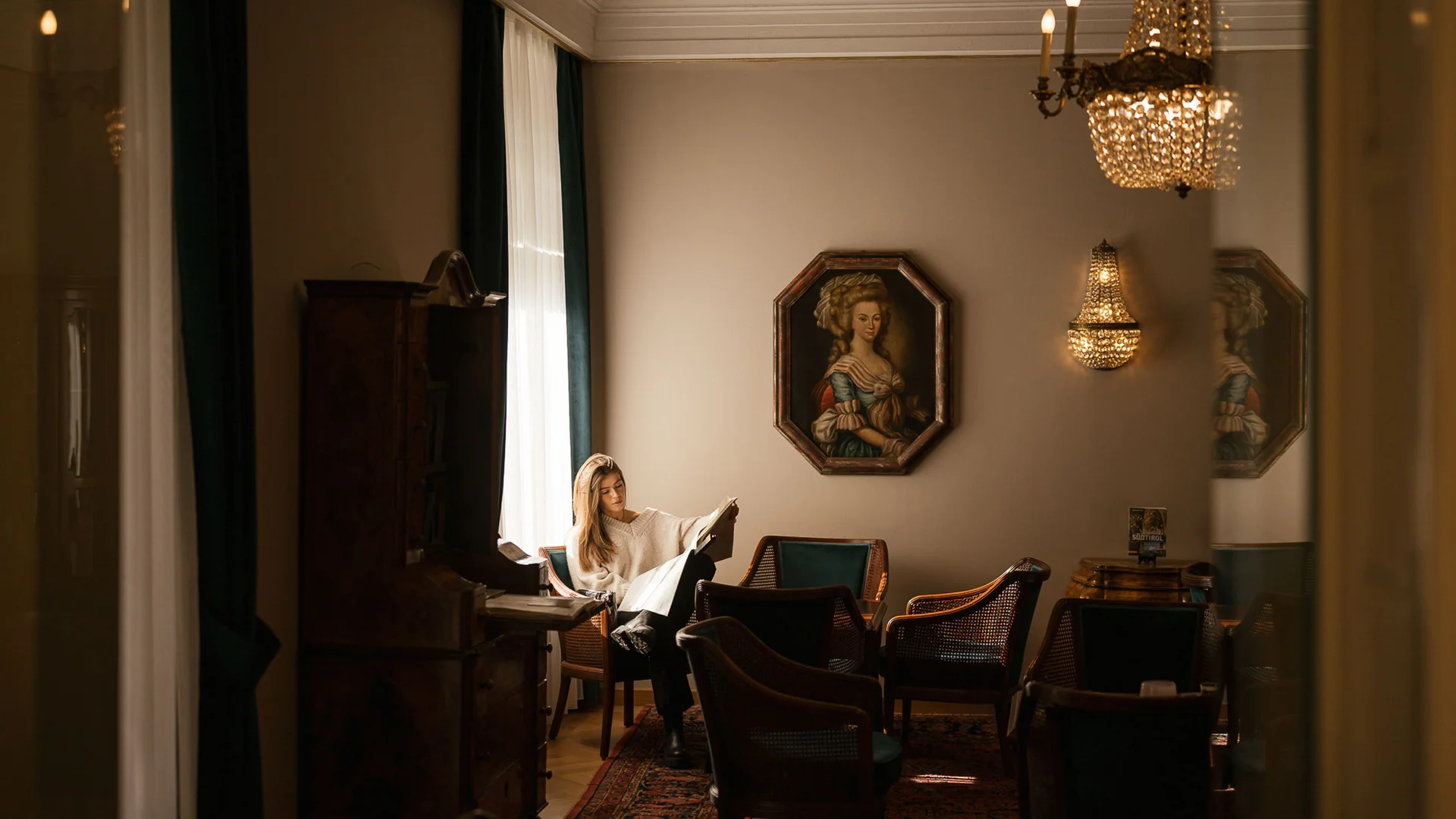Frau liest Zeitung in elegant eingerichtetem Raum mit Kronleuchter und Porträt