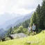 Two people hiking on green meadow with mountain scenery in background