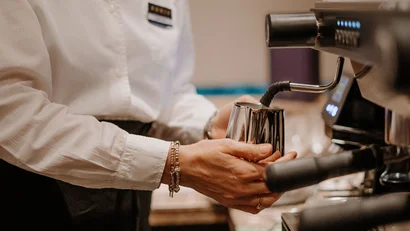 Person holding pitcher under coffee machine steam wand