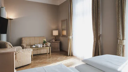 Bright hotel room with sofa, armchair, table, bed, and large windows