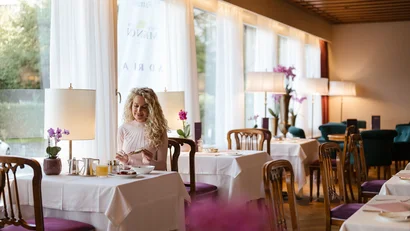 Woman eating in a bright, elegant restaurant with white tablecloths.