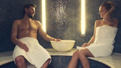 Man and woman relaxing in steam room wearing white towels