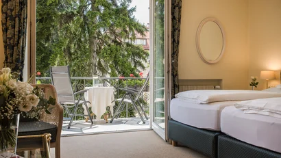 Hotel room with balcony, table and two chairs, view of trees